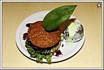 Hirschburger mit Ofenkartoffel (Hirschplanzl mit Blauschimmekäse überbacken auf buntem Salat mit karamellisiertem Zwiebel-Birnen-Ragout, geröstetem Speck und Smokey-Honey-Sauce im Roggenweckerl)